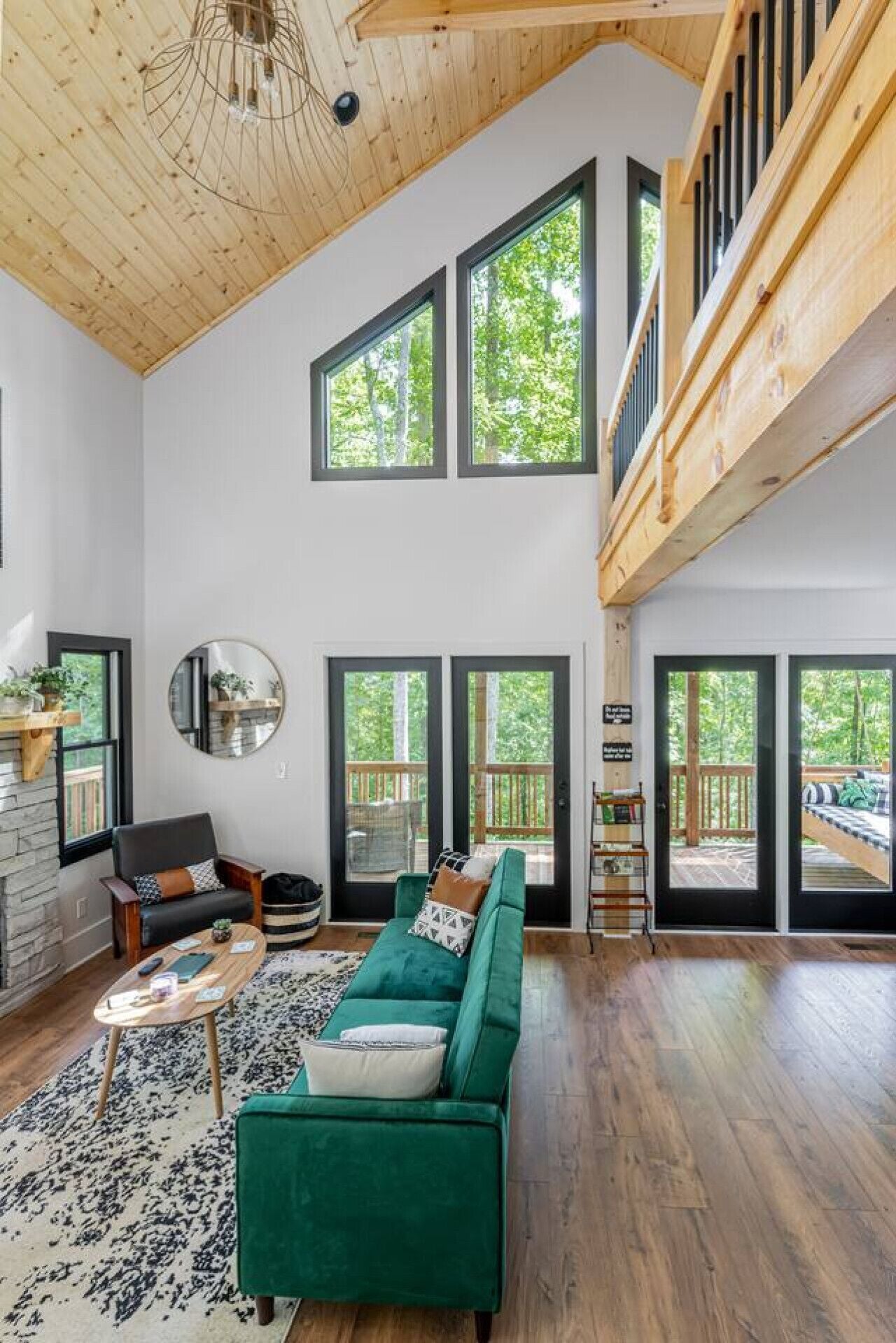 A spacious living room with a green sofa, a round mirror, and a wooden ceiling.