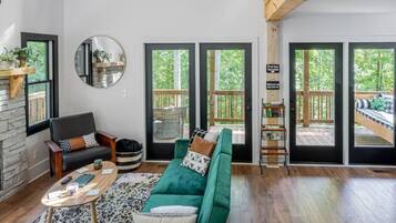 A spacious living room with a green sofa, a round mirror, and a wooden ceiling.