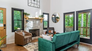 Una sala de estar con chimenea, un sofá verde, un sillón marrón y suelo de madera.