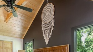 Un dormitorio con una cama grande, ventilador de techo, un tapiz de macramé y vistas al verdor exterior.