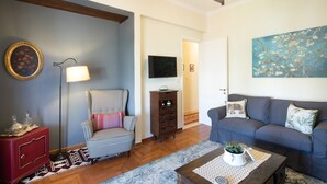 Un salon avec un fauteuil à motifs à carreaux, un canapé bleu, un meuble en bois et un lampadaire.