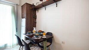 Un coin repas avec une table dressée pour deux personnes, un réfrigérateur et une étagère au-dessus de la table.