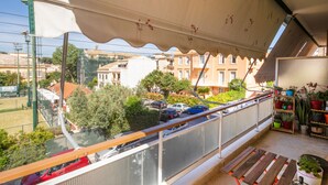 Un balcon donnant sur des voitures garées et des immeubles, avec une table et des plantes en pot.