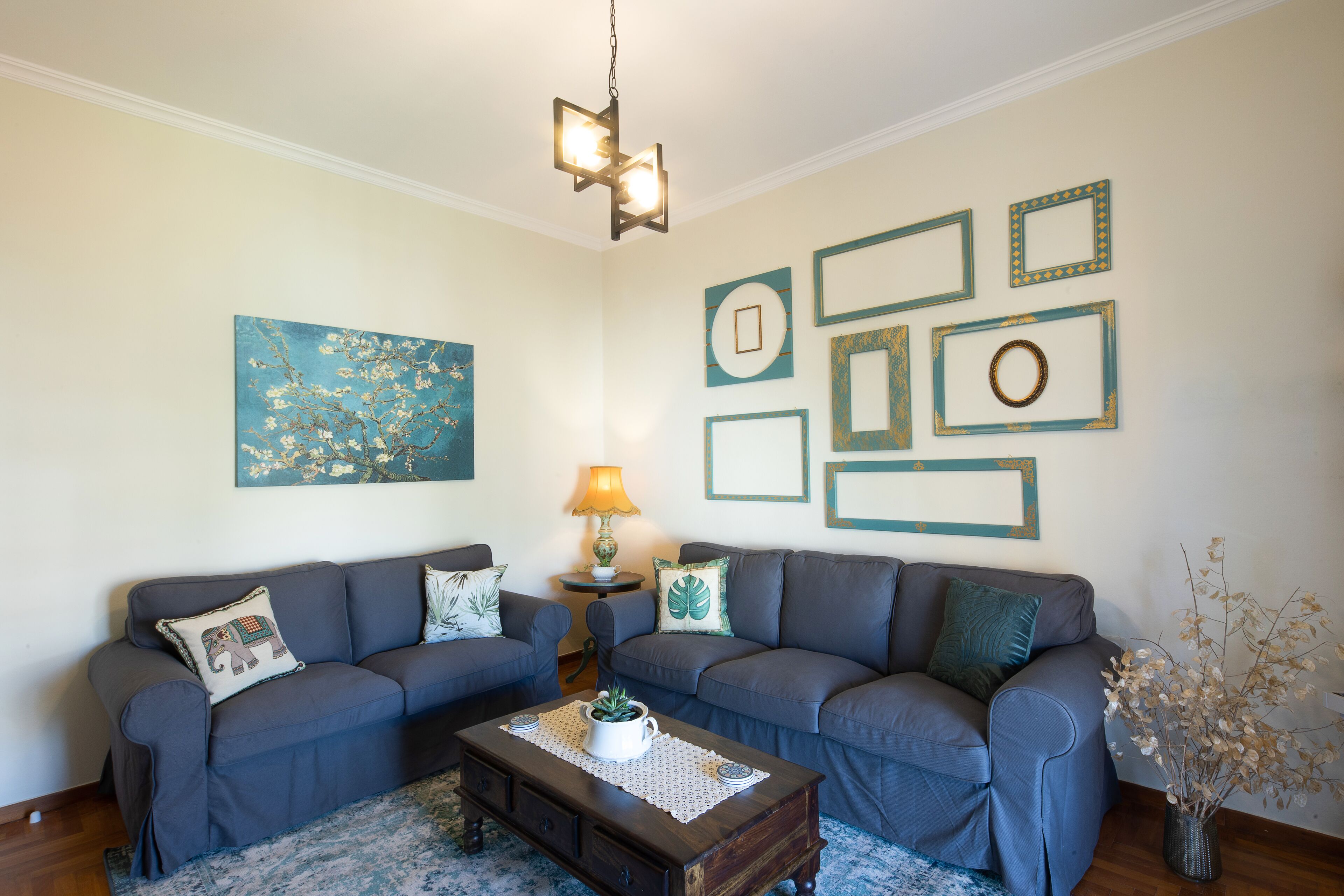 A living room with two grey sofas, a wooden coffee table, a blue rug, a wall-mounted lamp, and framed pictures.