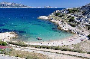 Ein Küstenstrand mit klarem türkisblauem Wasser, felsigem Gelände und einer kurvenreichen Straße.