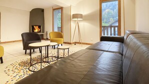 Een woonkamer met een open haard, een bank, een gele fauteuil en een vloerlamp.