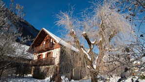A wooden cabin with a balcony, surrounded by snow-covered trees and a mountain in the background. - Magnificent detached chalet★7 bedrooms★prox. Alpe d'Huez (LE BOURG D'OISANS)