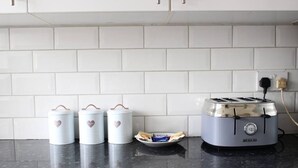 Uma bancada de cozinha com uma torradeira, três recipientes brancos com desenhos de coração e um prato com embalagens de lanches.