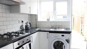 Uma cozinha compacta com fogão a gás, forno, máquina de lavar roupa e uma janela sobre a pia.