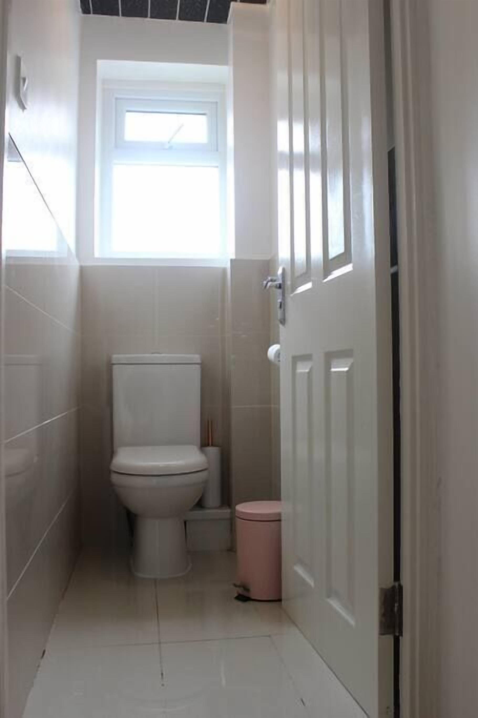 Un bagno piccolo e stretto, rivestito di piastrelle bianche, con il water, un cestino e una porta.