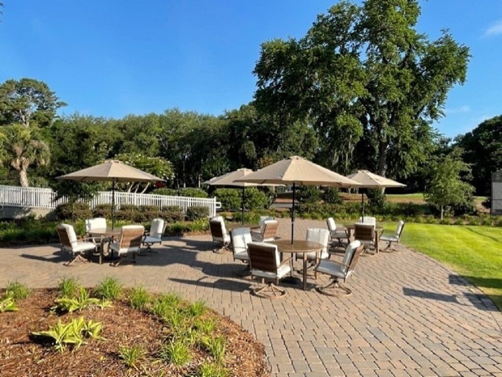 An outdoor patio with brick flooring, surrounded by lush greenery and trees.