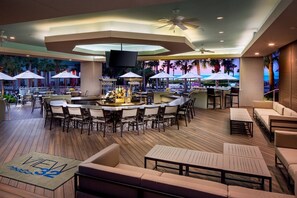 Een ruim buitengebied met een bar, met verschillende zitmogelijkheden, waaronder barkrukken en loungestoelen, en een groot scherm dat een schilderachtige panorama toont.