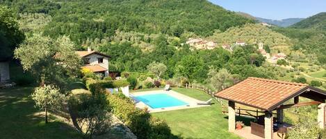 A villa with a swimming pool, surrounded by lush greenery and hills.