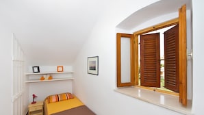 A bedroom with a bed, a nightstand, a shelf with pictures, and a window with wooden shutters. - A3 - Best Location in Center With the sea View (Vodice)