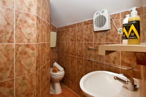 Un bagno con un WC, un lavandino e una doccia. Si vede un portasciuga, una doccetta e una bottiglia di shampoo sullo scaffale.