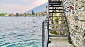 A concrete staircase leading down to a body of water, with a stone wall on one side and a view of buildings across the water. - VILLA MARIA by Design Studio (Bellano)