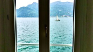 A view from inside a room with a large window overlooking a lake with a sailboat and mountains in the background. - VILLA MARIA by Design Studio (Bellano)