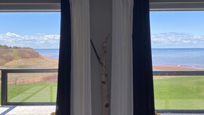 Une chambre avec vue sur l’Île-du-Prince-Édouard, avec une pancarte au-dessus d’une fenêtre ornée de rideaux blancs et foncés, une terrasse en bois et un bouleau au centre.