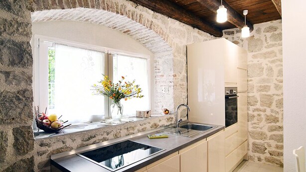 A kitchen with a stone archway, a window with flowers, and a modern sink. - Turrium Heritage Apartment con Patio e Camino Fronte Mare (Kaštel Kambelovac)
