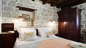 A bedroom with stone walls, a wooden wardrobe, a bed with white linens, and a nightstand with a lamp. - Turrium Heritage Apartment con Patio e Camino Fronte Mare (Kaštel Kambelovac)
