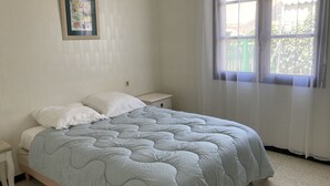 Una camera da letto con un letto, un comodino, tende leggere e un quadro appeso al muro.
