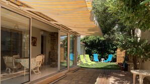Un patio coperto con tavolo e sedie, un pontile in legno e vista sul giardino con prato e poltrone relax.