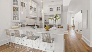 A spacious kitchen with white cabinetry, a large island with bar stools, and pendant lighting.