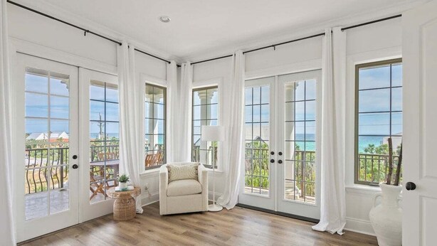 A spacious room with large windows offering ocean views, a comfortable chair, and a small table with a plant.