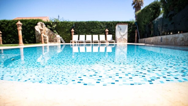 A swimming pool with a tiled floor, surrounded by white lounge chairs and a stone wall. - [✮✮✮✮✮ LUXURY VILLA WITH POOL] - Dimora Fanale (Torre Colonna-Sperone)