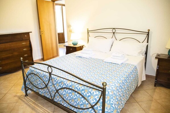 A neatly made bed with a patterned bedspread, a wooden dresser, and a bedside table with a lamp.