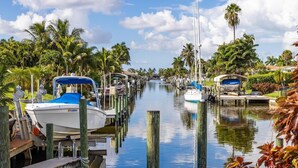 A marina with boats docked along a calm waterway, surrounded by lush greenery and palm trees. - Impressive Sunsets, Pet-friendly, Heated Pool- Nostra Palazzo on the Canal - Roelens Vacations (Cape Coral)
