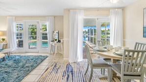 A bright dining area with a round table, white chairs, and a view of a pool and greenery outside. - Impressive Sunsets, Pet-friendly, Heated Pool- Nostra Palazzo on the Canal - Roelens Vacations (Cape Coral)