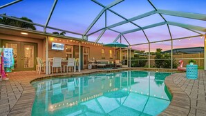 A covered outdoor pool area with a patio, chairs, and a table. - Impressive Sunsets, Pet-friendly, Heated Pool- Nostra Palazzo on the Canal - Roelens Vacations (Cape Coral)
