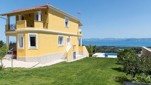 A two-story yellow house with a balcony, a swimming pool, and a view of the sea.