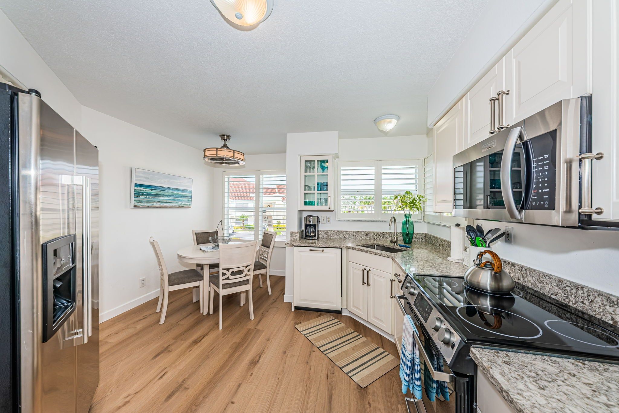 A modern kitchen with white cabinetry, a built-in oven, a microwave, and a dining area with a table and chairs.