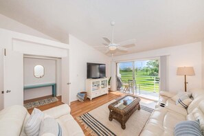 Uma sala de estar ampla com sofá, televisão, mesa de centro e varanda com vista.