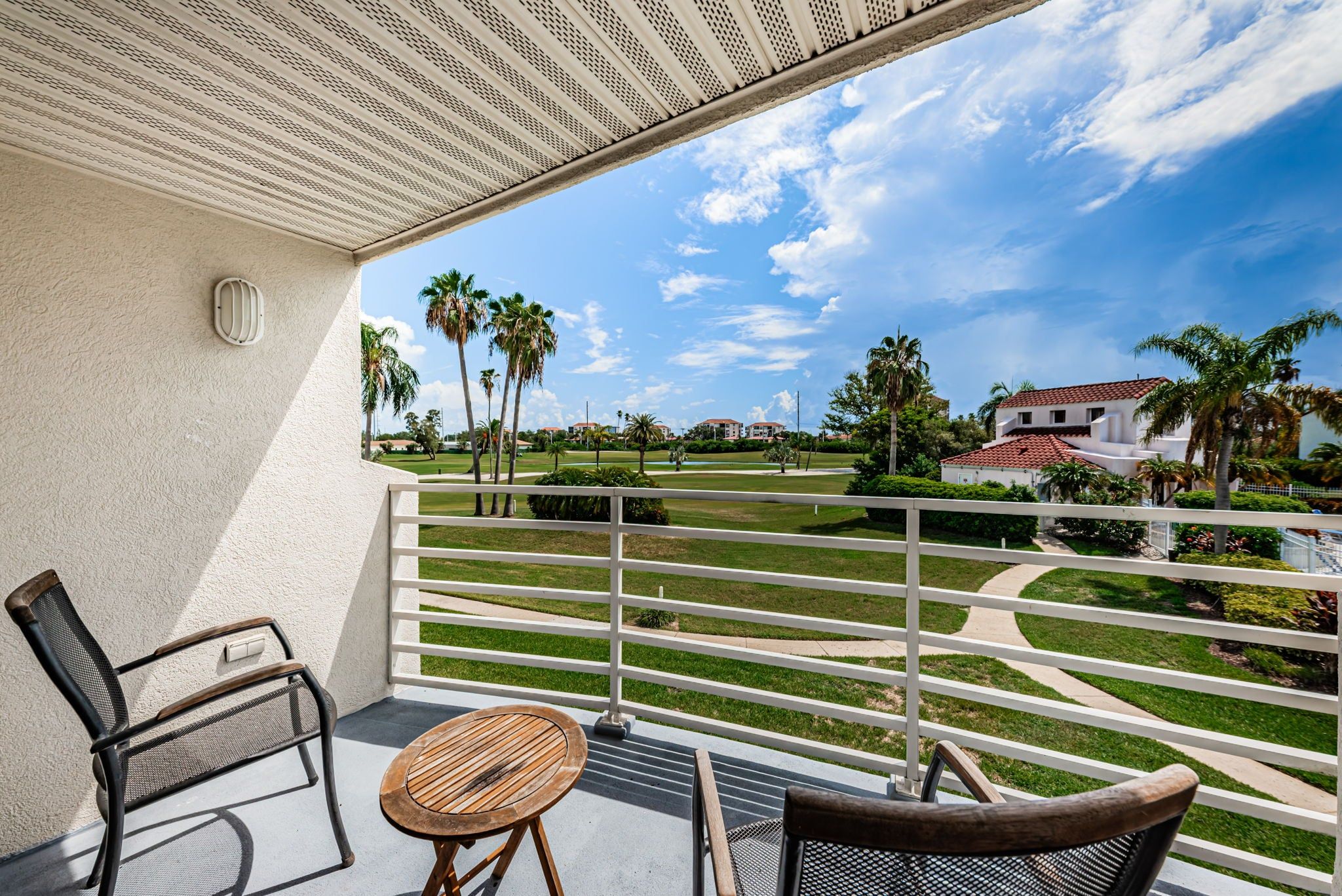 Un balcon avec vue sur un terrain de golf, des palmiers et un bâtiment doté d’un toit rouge.