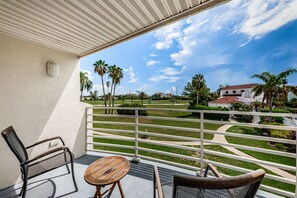 Un balcon avec vue sur un terrain de golf, des palmiers et un bâtiment doté d’un toit rouge.