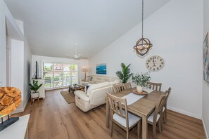 Un vaste espace de vie comprenant un canapé, une table à manger et des chaises, un ventilateur de plafond et une vue dégagée grâce à de grandes fenêtres.