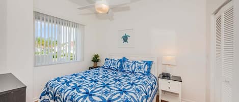 A bedroom with a bed, a nightstand, a ceiling fan, a window with blinds, and a door with louvered shutters.
