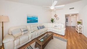 Ein Wohnzimmer mit einem weißen Sofa, einem Couchtisch, einem Deckenventilator und einem Bild an der Wand.