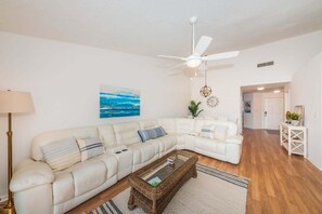 Ein Wohnzimmer mit einem weißen Sofa, einem Couchtisch, einem Deckenventilator und einem Bild an der Wand.