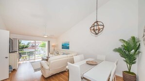 Ein modernes Wohnzimmer mit einem weißen Sofa, einem Esstisch und Stühlen, einem Deckenventilator und einer Hängelampe.