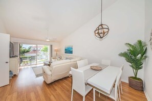Ein modernes Wohnzimmer mit einem weißen Sofa, einem Esstisch und Stühlen, einem Deckenventilator und einer Hängelampe.