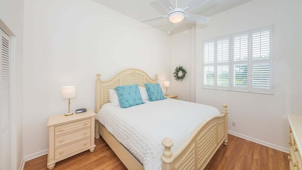 Ein Schlafzimmer mit einem Bett, Nachttischen, einem Deckenventilator und einem Fenster mit Jalousien.