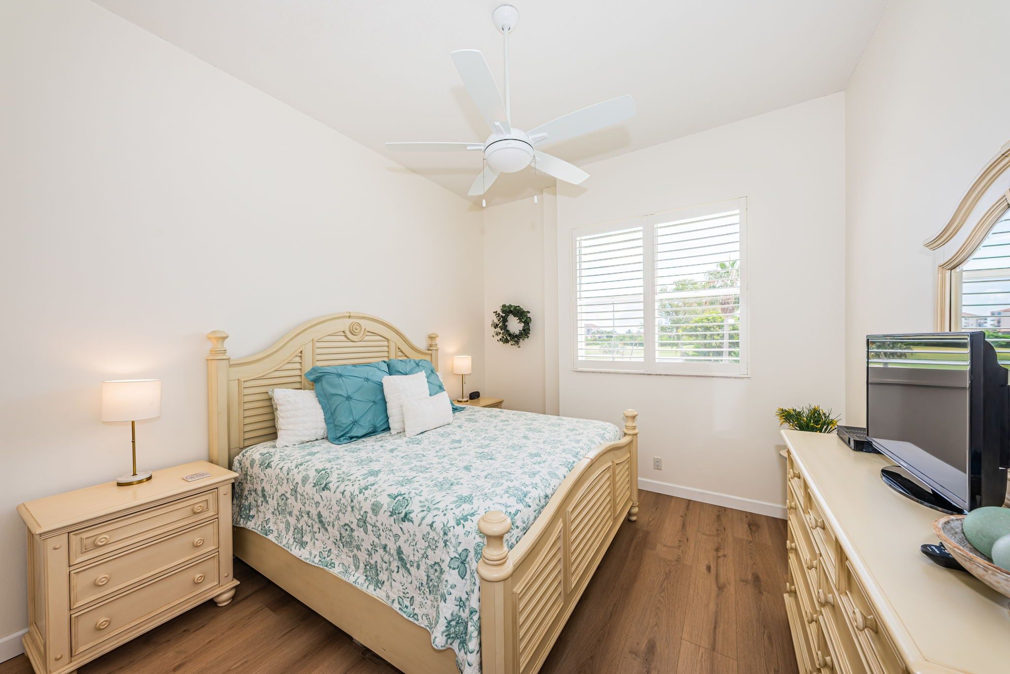 A bedroom with a bed, bedside tables, a desk, a ceiling fan, and a window with blinds.