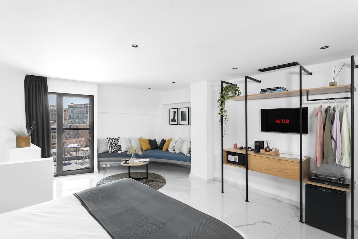 Una habitación de hotel moderna con cama, sofá, televisión, escritorio y balcón con vista a la ciudad.