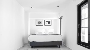 A modern bedroom with a large bed, a bathtub, and a window with a view.