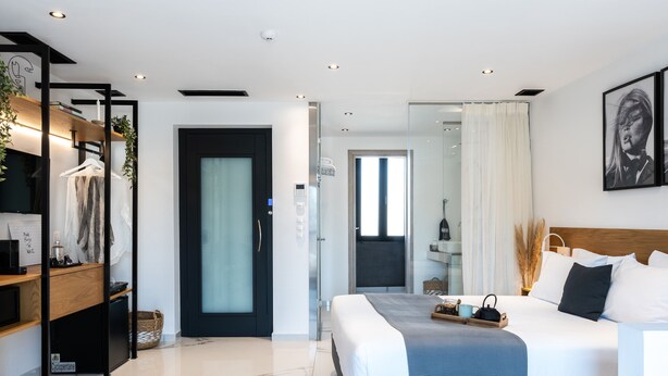 A modern hotel room with a bed, a wardrobe, a desk, and a bathroom visible through a glass door.
