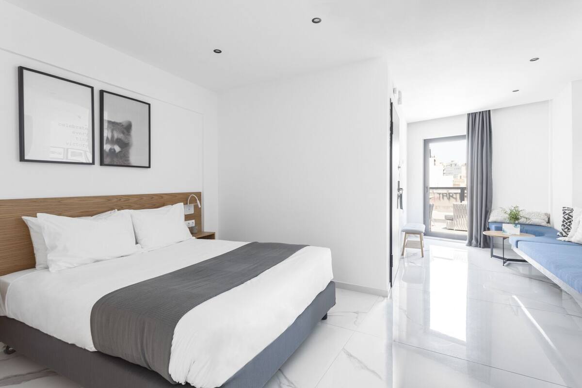Una habitación de hotel moderna con una cama grande, un pequeño rincón de descanso y un balcón con vistas.